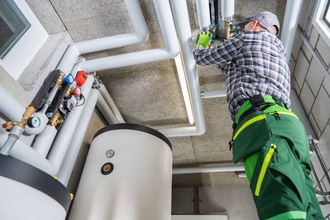 Plumber installing water heater and overhead pipe system